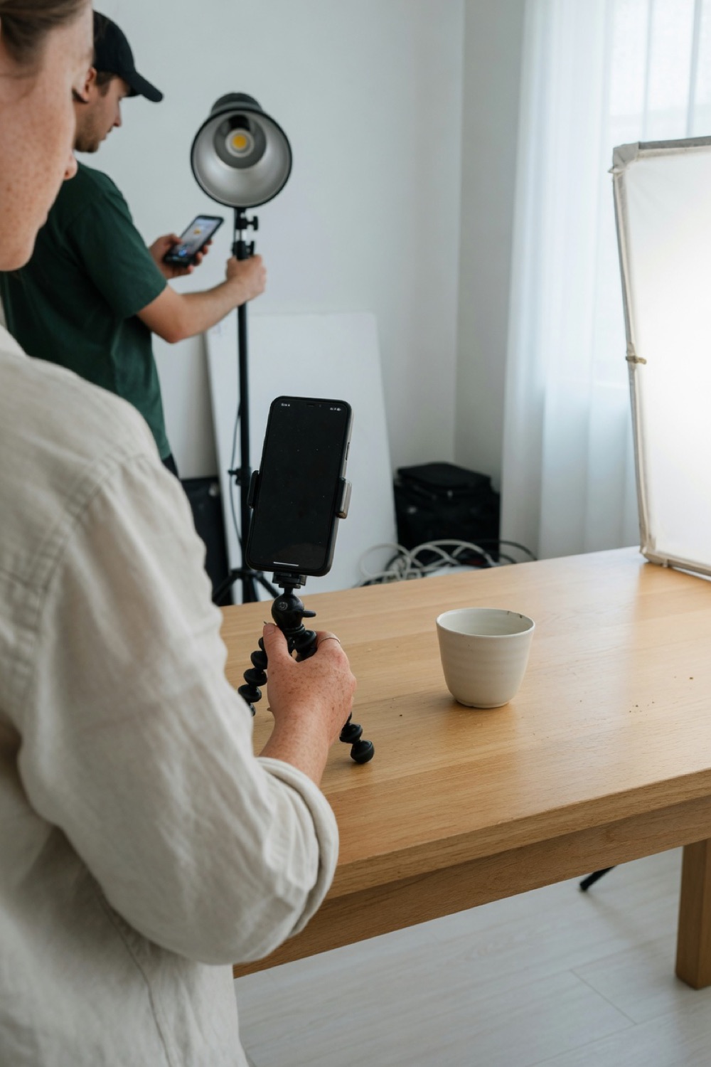 A person aiming a phone on a tripod at a cup on a wood table.